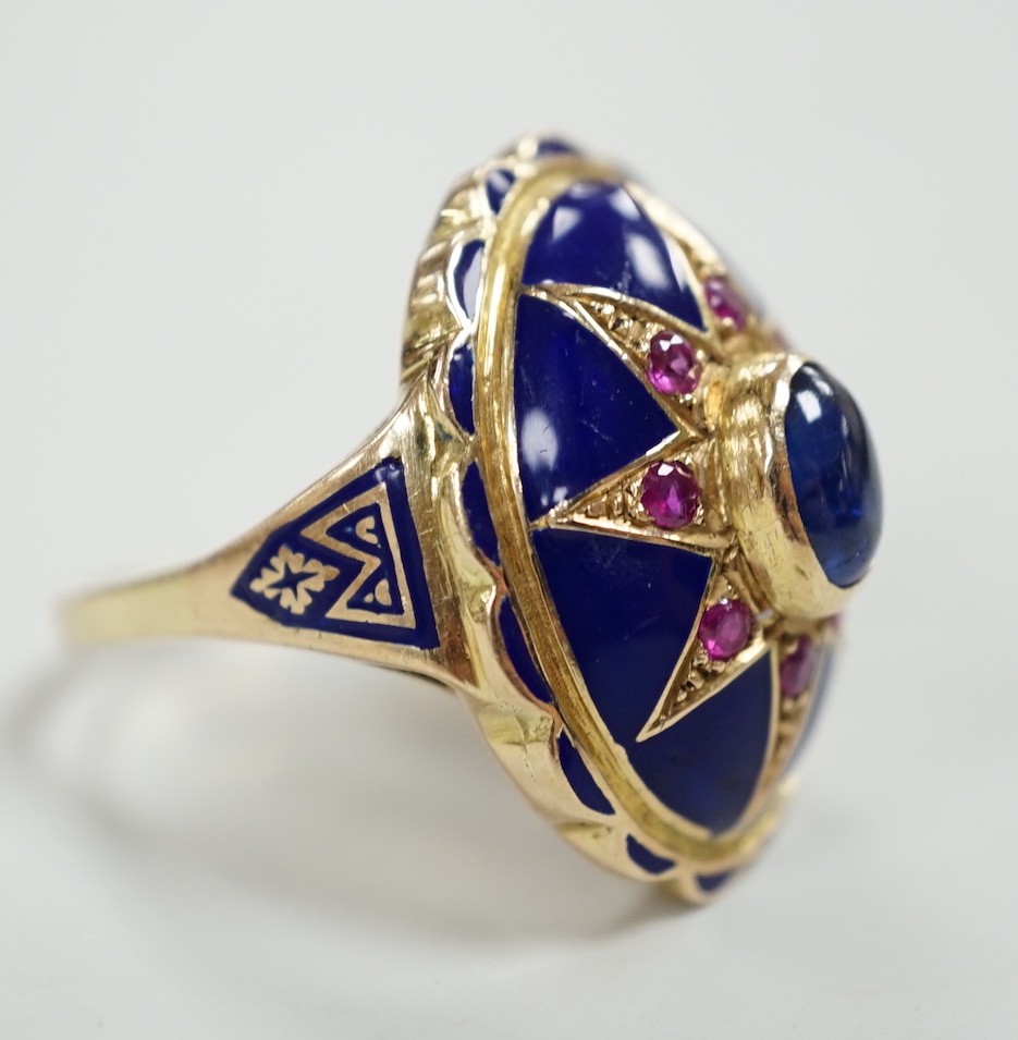 A yellow metal, blue enamel, ruby and cabochon sapphire set oval dress ring, the shank inscribed 'Sister My Sister?' size O, gross weight 13.7 grams.